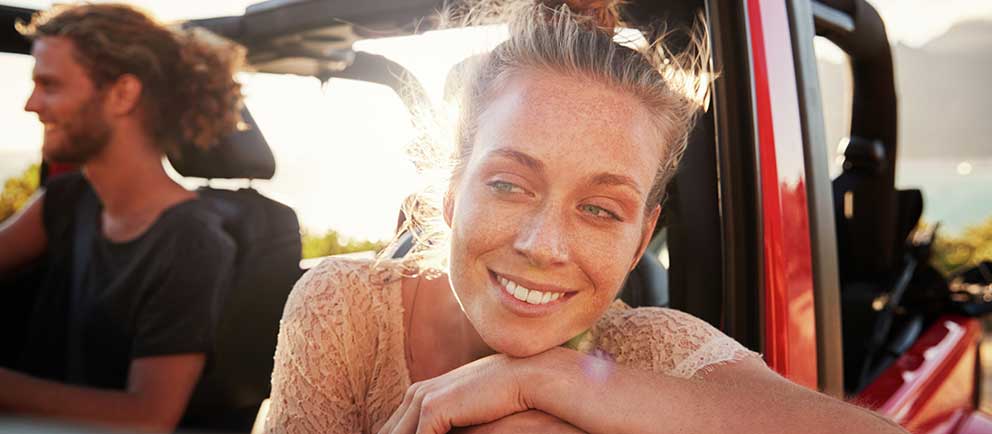 Smilende kvinne lener seg ut av vinduet i en bil