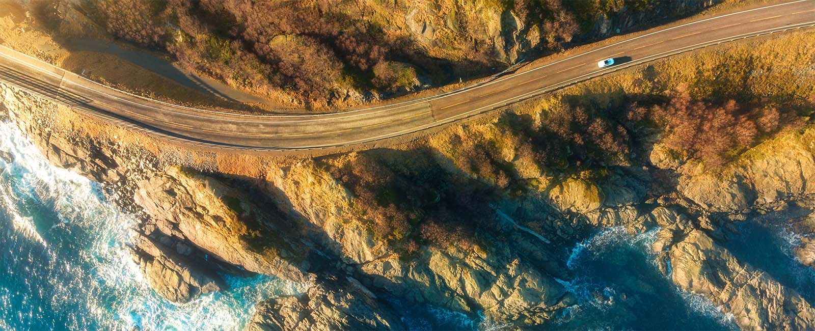 Flyfoto av bil som kjører langs fjellvei og sjø
